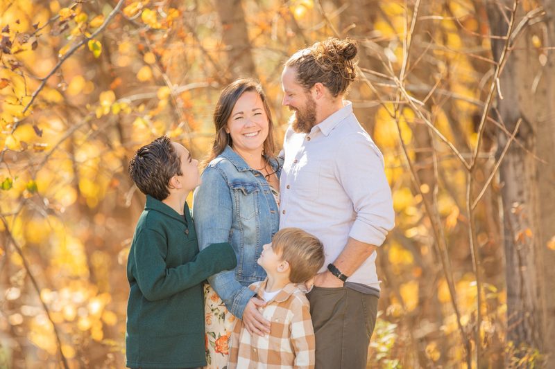 A family of four laughs together among bright yellow fall leaves