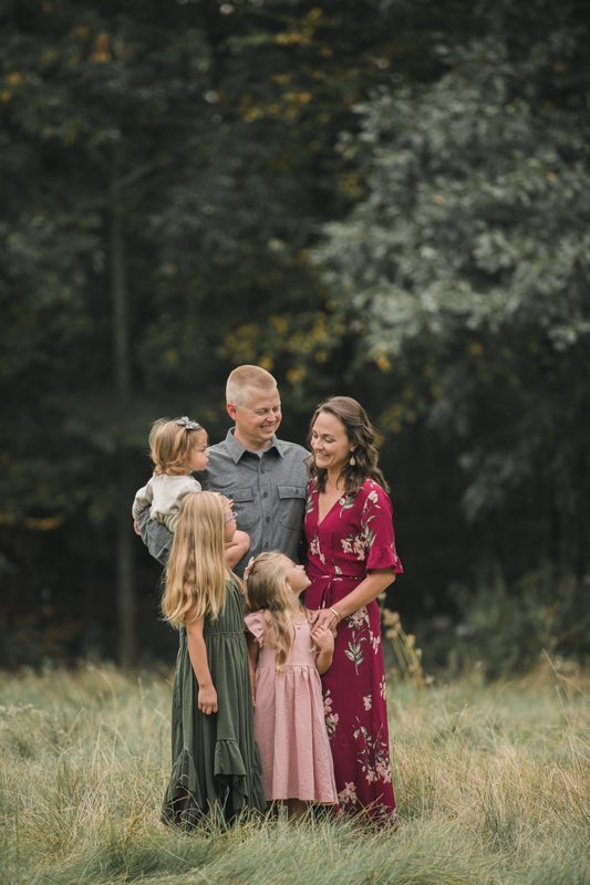 A family of five in a tall-grass meadow, mom in a red dress