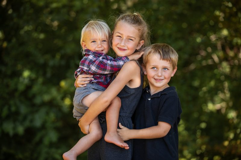A big sister carries her little brother as another brother leans in, all smiling
