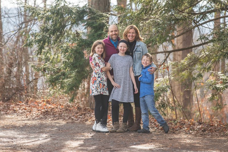 A family of five stands close together on a leafy forest trail