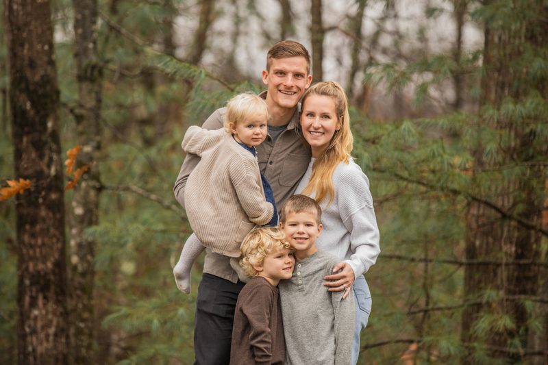 A mom and dad hold their three little boys close in a misty pine forest