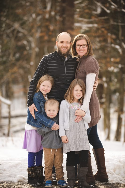 A family with four children stands together in the snowy woods