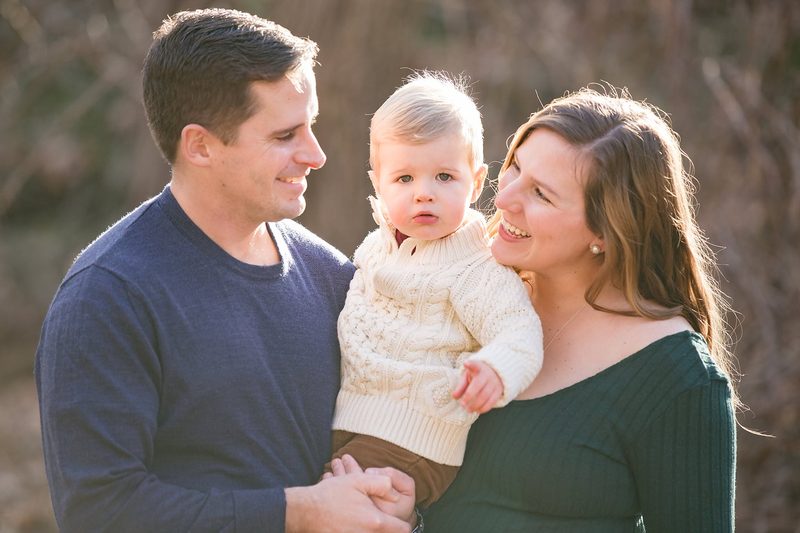 Parents smile at their toddler son in a cream cable-knit sweater