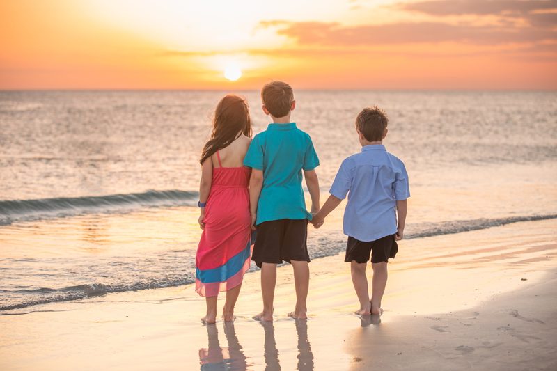 Three kids hold hands on the beach at sunset