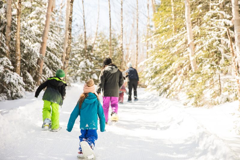 Kids snowshoe single file along a snowy forest trail